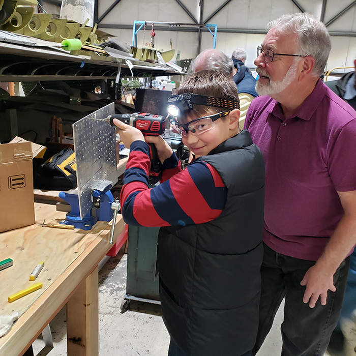 Volunteer helping a child drill a metal plate