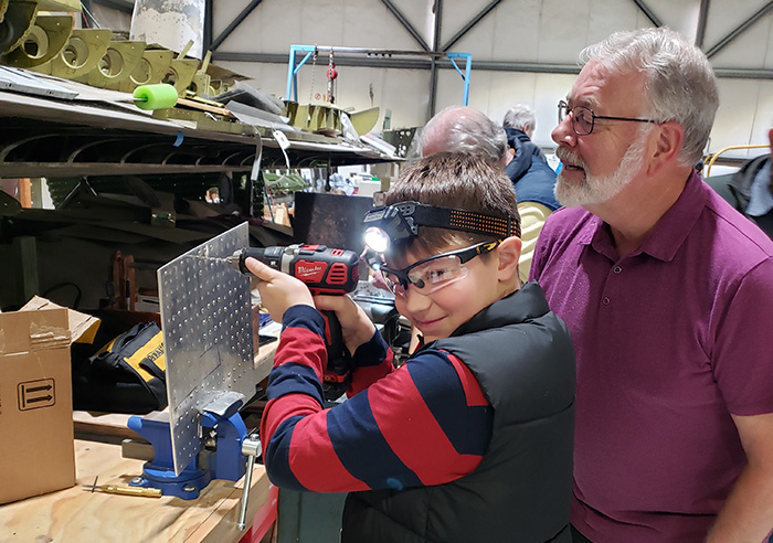 Volunteer helping a child drill a metal plate